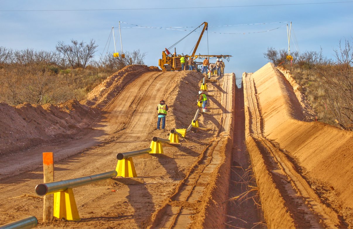 KES crew lowering pipe into the trench with a sideboom during a pipeline construction project